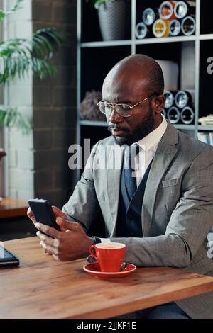 African businessman concentrating on his online work on mobile phone sitting at table and drinking coffee at the cafe Stock Photo