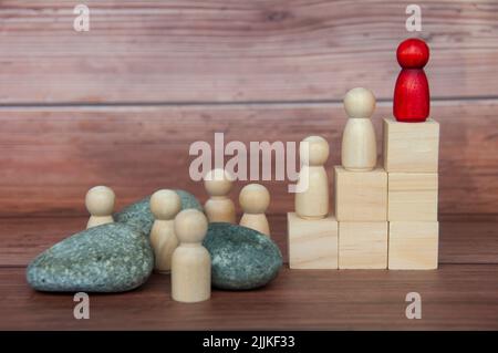 Red wooden doll on top of wooden block with others having to face challenges along the way. Goal achieving and leadership concept Stock Photo