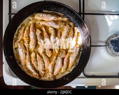 top view of frying breaded Black Sea surmullet fishes in old round cast-iron frying pan on gas stove in rustic kitchen Stock Photo