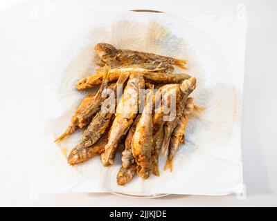 top view of portion fried small Black Sea red mullet fishes on white paper napkin in plate on white table Stock Photo