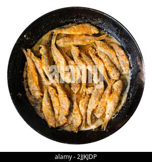 top view of fried small Black Sea red mullet fishes in old round cast-iron frying pan cutout on white background Stock Photo