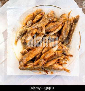 top view of portion of fried small Black Sea surmullet fishes on white paper napkin in plate on wooden table Stock Photo