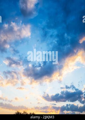 sunlit gray clouds in dark blue sky at summer sunset Stock Photo