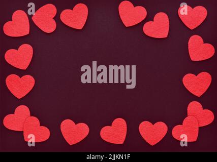 Background for your greetings for a Valentine's day. Frame with red felt hearts on dark red paper. Top view Stock Photo