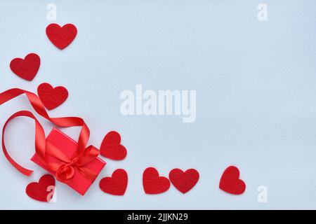 Valentines Day background. Red gift box with ribbon and felt hearts on a pastel blue background. Top view Stock Photo