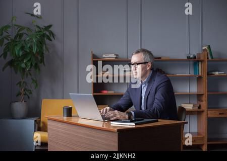 Serious pensive thoughtful focused business accountant bookkeeper in office looking at and working with laptop and income tax Stock Photo