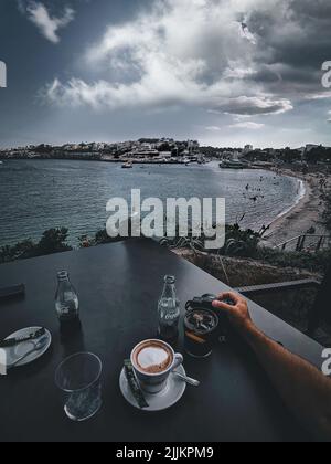 A close-up shot of a cup of coffee and two bottle of Coke on a table with a beautiful seascape on a background Stock Photo