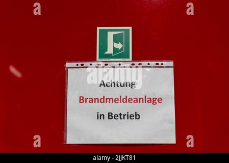A "Warning Fire alarm system in operation" banner in German on a red wall Stock Photo