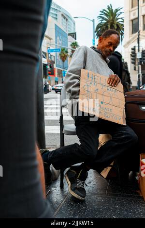 The vertical shot of an homeless black elder man homeless person holding a sign asking for money Stock Photo