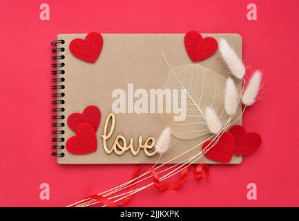 Background for your greetings for a Valentine's day. The word "Love" with the notebook and felt hearts on the red background. Top view. Stock Photo