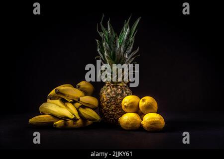 A closeup shot of bananas, pineapple, and lemons on black background Stock Photo