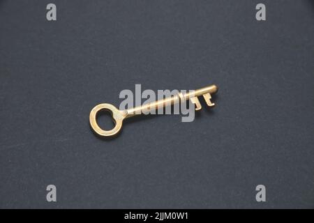 A closeup of a golden key isolated on dark gray background. Stock Photo
