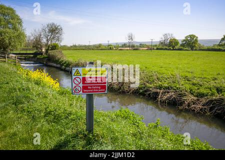 A sign warning of the dangers of the overhead electricity cables on the bank of the River Yeo, also known as the Congresbury Yeo, at Iwood near Congresbury, North Somerset, England. Stock Photo