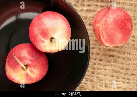 Three sweet nectarines in a black ceramic dish on jute fabric, macro, top view. Stock Photo