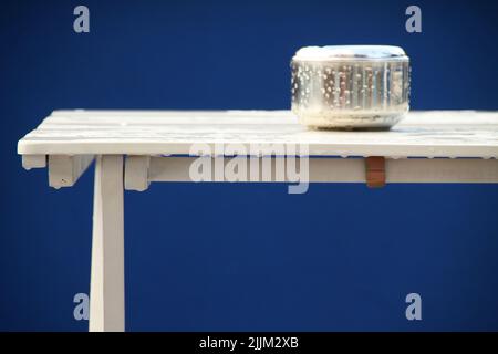 A wet ashtray on a wet white table against a blue background Stock Photo