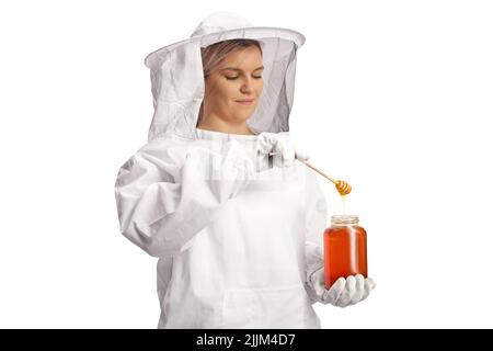 Female bee keeper taking dipping a wooden dipper in a jar of honey isolated on white background Stock Photo