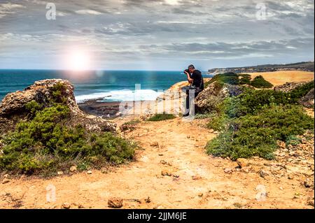 A male photographer capturing scenic seascape view under a cloudy sky Stock Photo