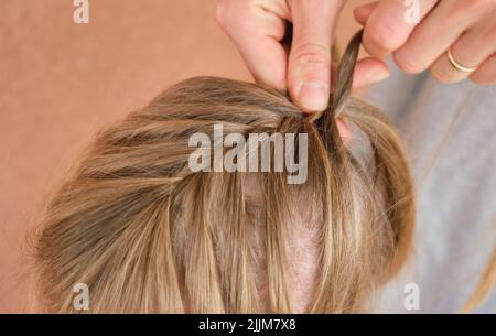 Mother combs her daughters hair and braids it at home little girl with long hair Stock Photo