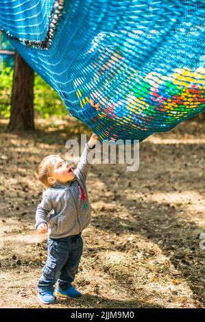 A vertical closeup of a small boy touching a safety net with plastic balls of an obstacle route in Pyrland Park. Stock Photo