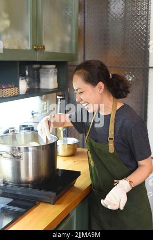 Young Vietnamese woman stirring  dough in a big metal saucepan Stock Photo