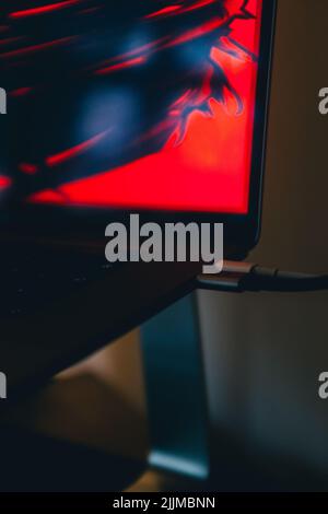 A vertical closeup of a laptop with a red neon wallpaper Stock Photo