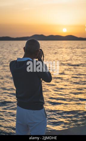 A back view of a middle-aged man taking a picture of a beautiful sunset in Croatia Stock Photo