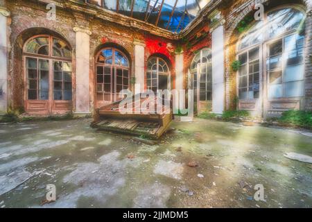 A broken old wooden grand piano in the middle of an abandoned building and sunlight shining through windows Stock Photo