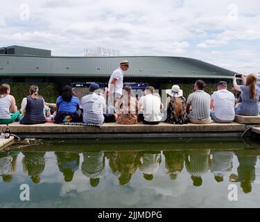 Wimbledon Tennis Championship. Spectators sitting on the edge of a pond at The Hill outside number one court. London Stock Photo