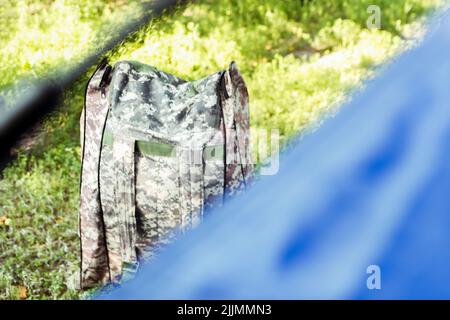Defocus blue open tourist tent standing on green nature background. Army backpack. Tourism concept. Summer vacation in forest, camping. Blurred. Hunte Stock Photo
