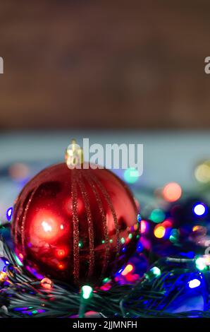 A close-up shot of a red Christmas ball on a string of colorful lights  with a blurred background Stock Photo