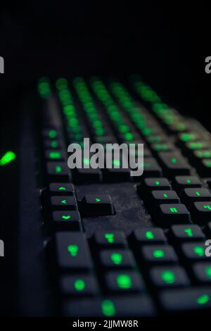 A vertical shot of a keyboard with green lights in the dark Stock Photo