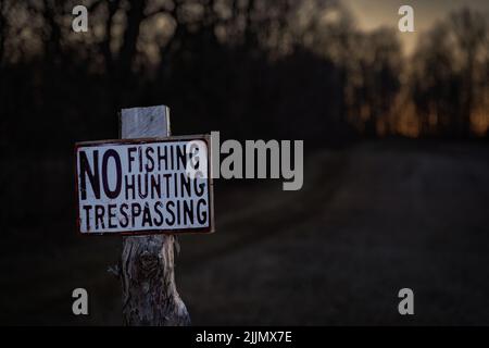 A closeup shot of a sign of 'NO FISHING HUNTING TRESPASSING' on a wood side of the road Stock Photo