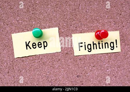 Keep fighting words on stick note and blue pinned to a cork notice board. Business concept. Stock Photo