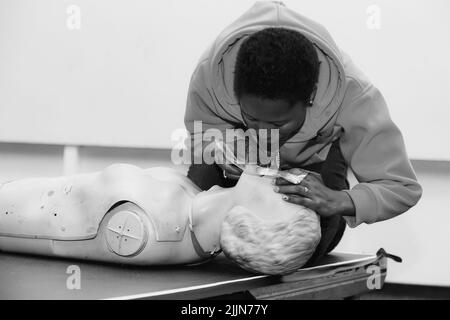 A grayscale shot of a person doing first aid CPR training with a plastic dummy Stock Photo