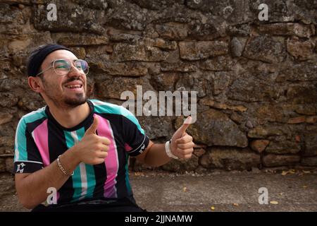 A young guy with beard, eyeglasses, braids in his hair and headband smiling making the ok symbol with his hands Stock Photo