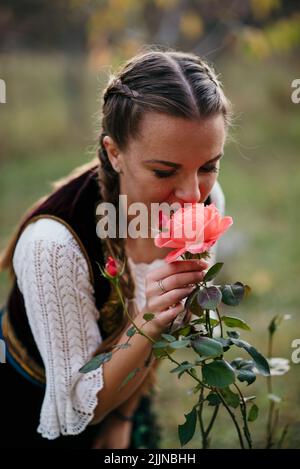 A closeup of golden hair girl in Serbian traditional costume smelling rose Stock Photo