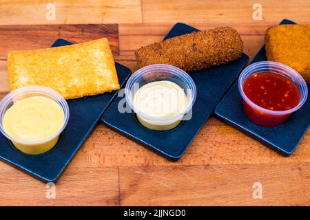 A top view of deeply fried nuggets with different types of sauces on a wooden board Stock Photo