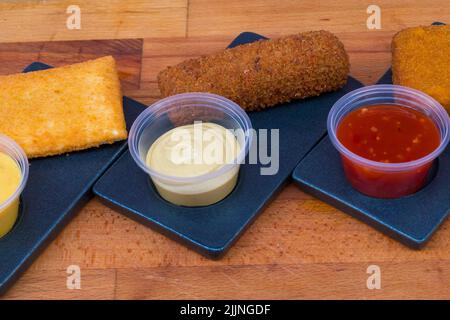 The different types of deep-fried crunchy nuggets with sauces on a black plate Stock Photo