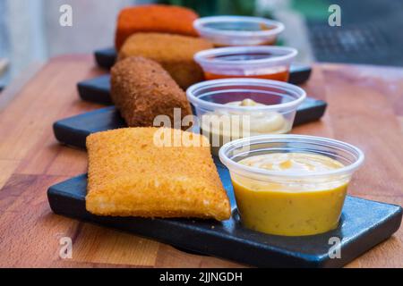 A selective focus shot of a crispy deep-fried nugget along with a cheese sauce on a wooden board Stock Photo