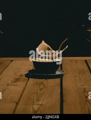 A vertical closeup shot of a mug of cappuccino with coffee spilling out on the wooden table Stock Photo