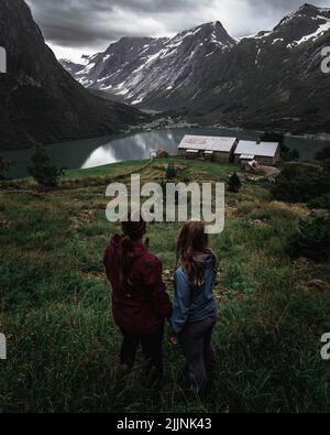 A back view of two girls standing in the grass field and looking at views of Segestad Norway Stryn Stock Photo