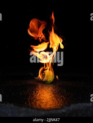 A vertical closeup shot of the burning tennis ball on the black background Stock Photo