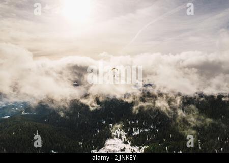 The paraglider floating against the white clouds above the green hills. Stock Photo