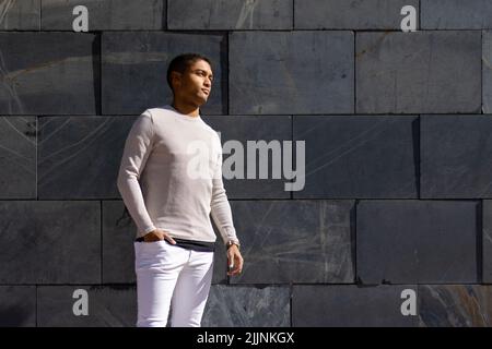 A Hispanic man posing in trousers and a white pullover, horizontal flagstone background Stock Photo