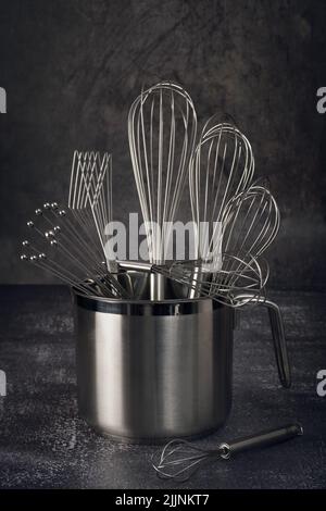 A closeup shot of metal baking utensils set in a container put on a kitchen table Stock Photo