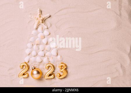 Creative Christmas tree made of shells and symbolic numbers of new year 2023 background of sea sand Stock Photo