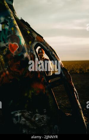 A vertical shot of a man seen through the window of a colorful car at Cadillac Ranch in Amarillo, Texas Stock Photo