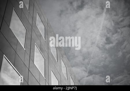 A low angle shot of a modern building under a cloudy sky in grayscale Stock Photo