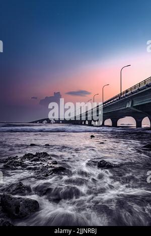 A vertical shot of a bright sunset sky over a bridge near the shore Stock Photo