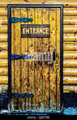 Grungy wooden door in log cabin with decorative rustic hinges and carved wooden sign that says Entrance Stock Photo